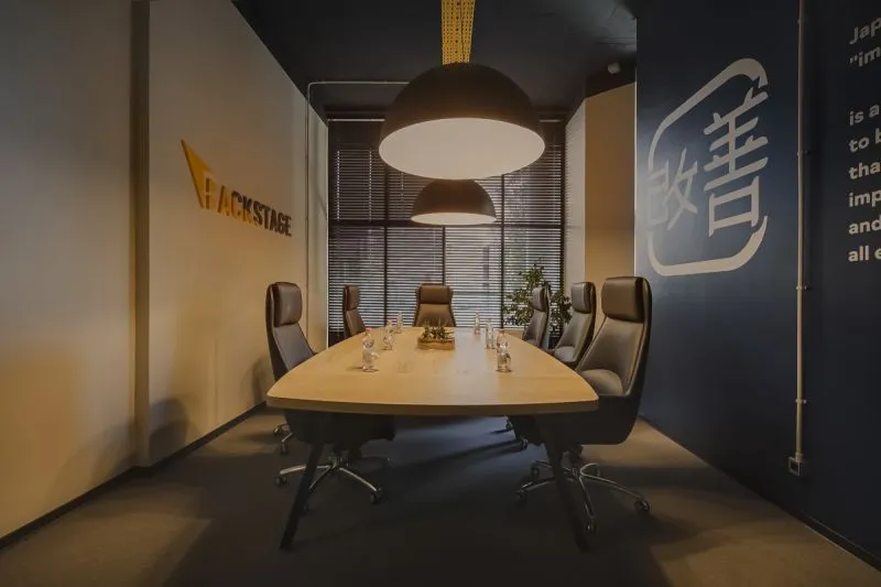 Een vergaderruimte met een houten tafel, zwarte stoelen en het Backstage-logo aan de muur.