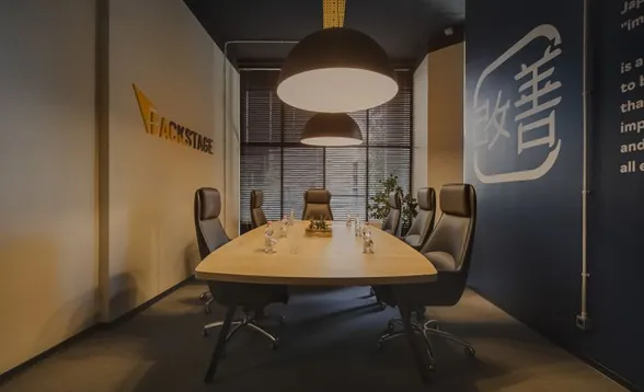 Lege vergaderruimte met een lange houten tafel, zwarte leren stoelen, twee bolvormige hanglampen, het Backstage-logo op de ene muur en een Japans kaizen-symbool op de andere