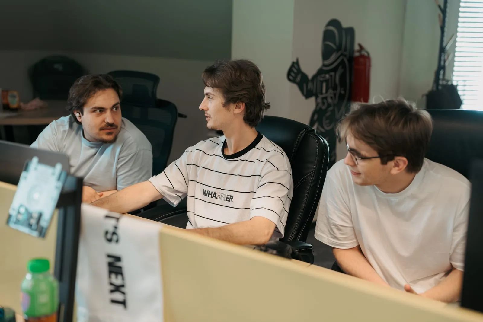 Drie developers van Backstage IT achter hun bureaus op kantoor in Chișinău, met een banner van What’s Next op de scheidingswand achter hen.
