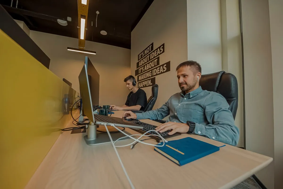 Twee developers aan het werk op kantoor bij Backstage IT, onder een muurtekst over ideeën waarmaken.