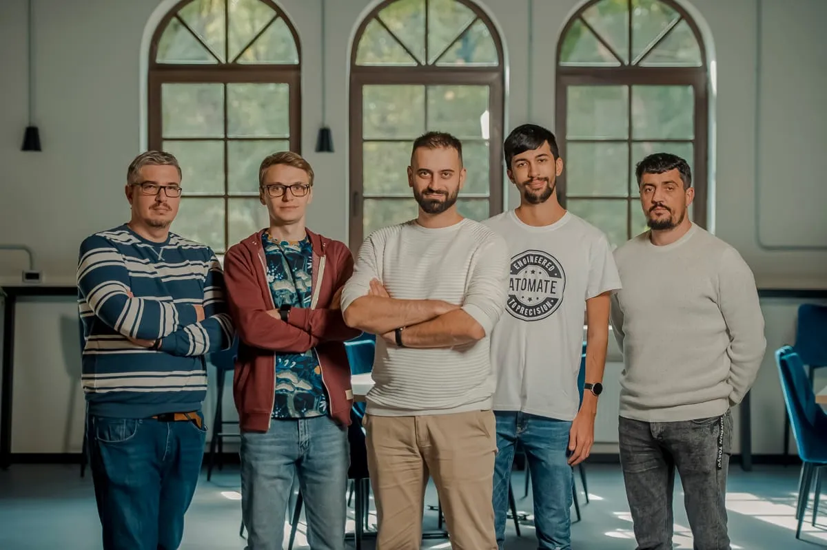 Vijf teamleden van Backstage IT staan naast elkaar in een kantoor met hoge boogramen.